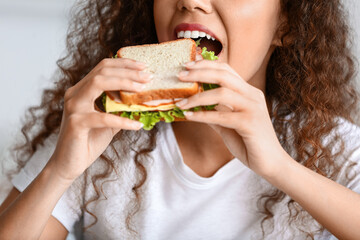 Young African-American woman eating tasty sandwich at home, closeup
