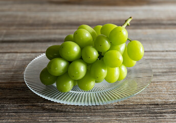 Wall Mural - Shine Muscat grapes on a glass plate set against a wooden background.