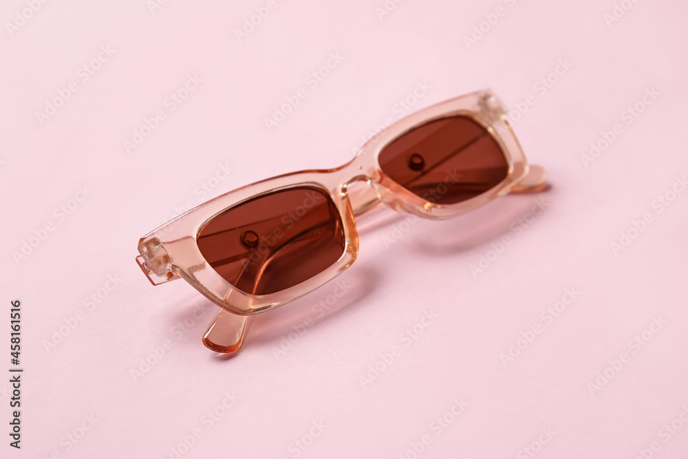 Stylish female sunglasses on color background