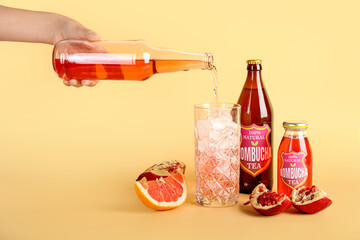 Wall Mural - Woman pouring tasty kombucha tea from bottle into glass on color background