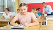 © JackF - Teen girl listening to lecturer and writing in notebook in classroom