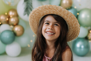 Closeup portrait of a beautiful smiling little dark-skinned girl with brown eyes and dark hair in a straw hat against the background of balloons. Concept of spring summer youth beauty. Beautiful face