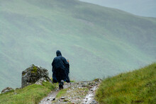 Along The West Highland Way. A Lonesome Hiker Protected By A Rain Cape Walks On The Hiking Path Under A Shower