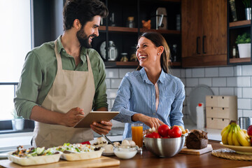 Wall Mural - beautiful young couple is using a digital tablet and smiling while cooking in kitchen at home