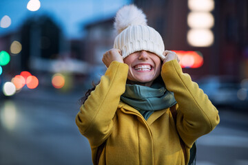 Young woman playing with winter cap on city street