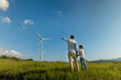 © Kitreel - Cinematic shot of carefree young father engineer keeping his daughter for hand and showing windmill field. Concept of renewable energy, love for nature, family, electricity, green, future.