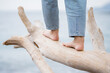 Caucasian woman feet walking on white wooden log on beach with sea