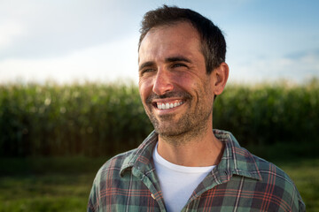 Cinematic shot of young male farmer is enjoying nature around and smiling satisfied with his work on countryside farm corn fields. Concept of agriculture, nature, cultivation, bio and eco farming.