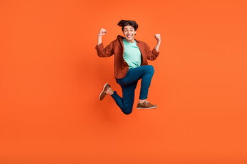 Poster - Full size photo of smiling cheerful young man jumping raise fists in victory triumph isolated on orange color background