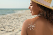 Beautiful African American woman with sun protection cream on shoulder at beach