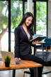 © amnaj - Young Asian businesswoman sitting at her desk using a laptop keyboard holding a notebook at the office.