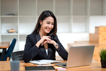 Happy young Asian businesswoman sitting at the office using laptop with document at the desk.