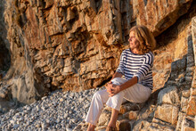 Mature Woman Resting On Rocky Coast Against Mount
