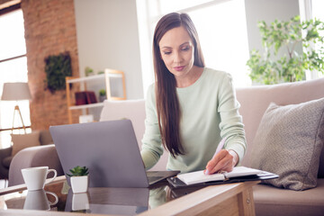 Poster - Photo of thoughtful shiny mature lady wear teal pullover smiling sitting couch writing copybook modern gadget indoors house room