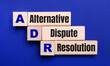 On a bright blue background, light wooden blocks and cubes with the text ADR Alternative Dispute Resolution