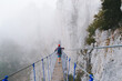 A young man in mountaineering equipment walks uphill on a suspension bridge in the fog. Suspension bridge on Mount Ai-Petri, Yalta, Crimea. The concept of travel, active lifestyle, tourism.