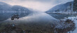 Beautiful mountain and lake winter panorama landscape of calm reflection on Kootenay Lake with sunrise or sunset light and mist in Nelson, British Columbia, Canada.