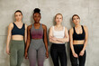 © Drazen - Group of young diverse sportswomen stand against the wall and looking at camera.