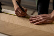 A designer man using his measuring tape to measure a piece of veneer wood and making furniture in his carpentry workshop studio