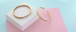 Panorama of Two modern golden bracelets on pastel colors paper background with copy space