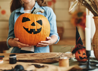 Little kid girl holding classic Jack O Lantern carved orange pumpkin with spooky face