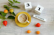 Calendar for October 31 : the name of the month in English, cubes with the number 31 , a yellow cup with hot coffee, branches of physalis with orange boxes on a gray background