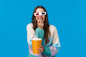 Cheerful and happy, laughing brunette caucasian girl enjoying funny movie, wearing 3d glasses, chuckling and munching popcorn, holding box, standing in winter sweater, cinema offer student dicsount