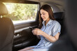 © geargodz - happy woman using a smartphone while sitting in the back seat of car