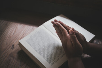 Wall Mural - Man with Bible praying, hands clasped together on her Bible on wooden table.