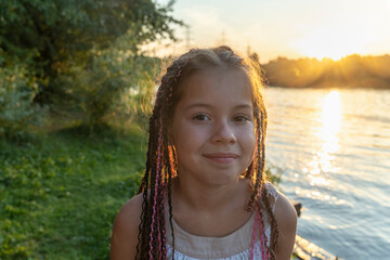 cute little girl with african pigtails on background of lake and beach in close - up looks mysteriou
