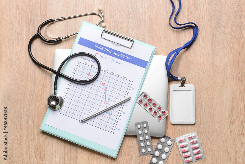 Audiogram with stethoscope, pills and badge on light wooden background