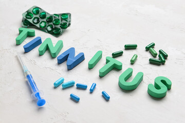 Word TINNITUS with pills and syringe on white background