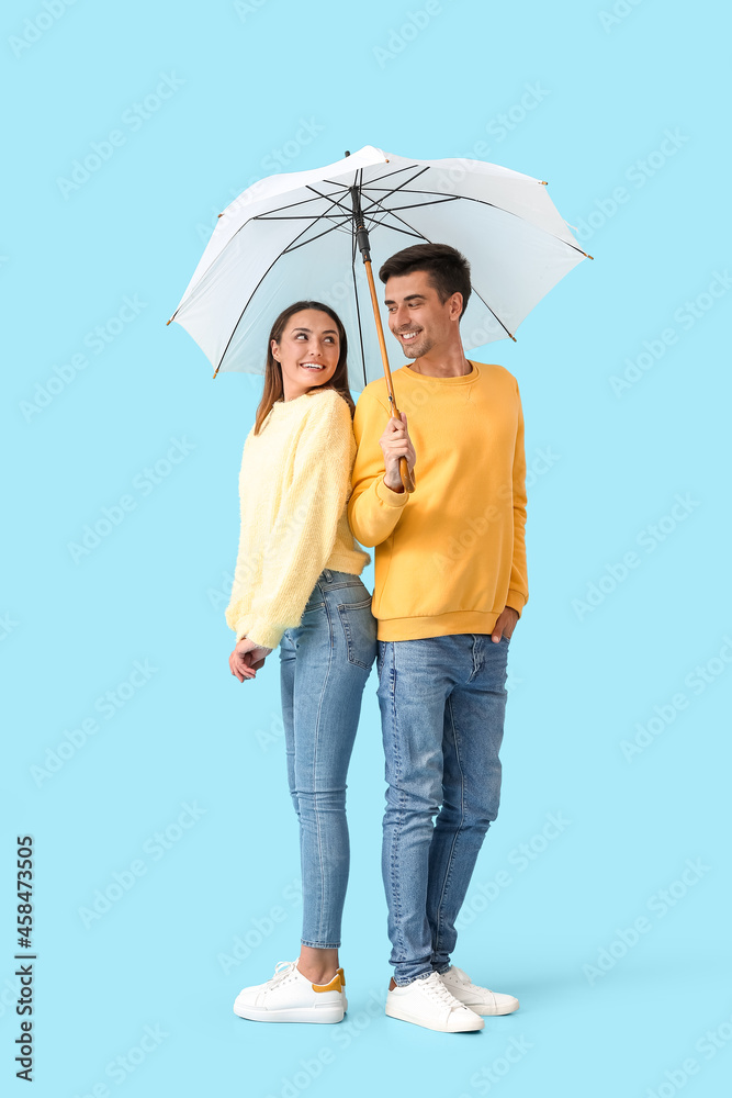 Young couple with umbrella on color background