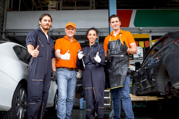 Wall Mural - Group of four car service technician men and woman giving thumbs up to camera, people working together at vehicle repair garage service shop, check and repair customer car at automobile service center