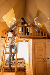 Wall Mural - Man pointing at laptop near asian girlfriend with cups in glamping house during vacation