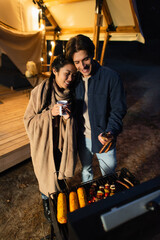 Wall Mural - Multiethnic couple with cup grilling food near glamping house