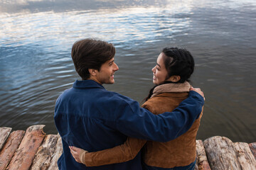 Wall Mural - side view of positive couple hugging on wooden pier near sea
