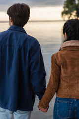 Wall Mural - back view of couple holding hands near blurred sea