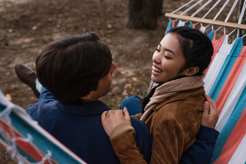 Wall Mural - Asian woman hugging boyfriend in blurred hammock during vacation