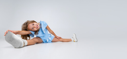 Beautiful little girl in blue holiday outfit sitting on floor isolated on white studio background. Happy childhood concept. Sunny child.