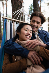 Wall Mural - Blurred man embracing asian girlfriend in hammock in autumn