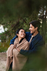 Wall Mural - Smiling interracial couple with blanket looking at each other outdoors