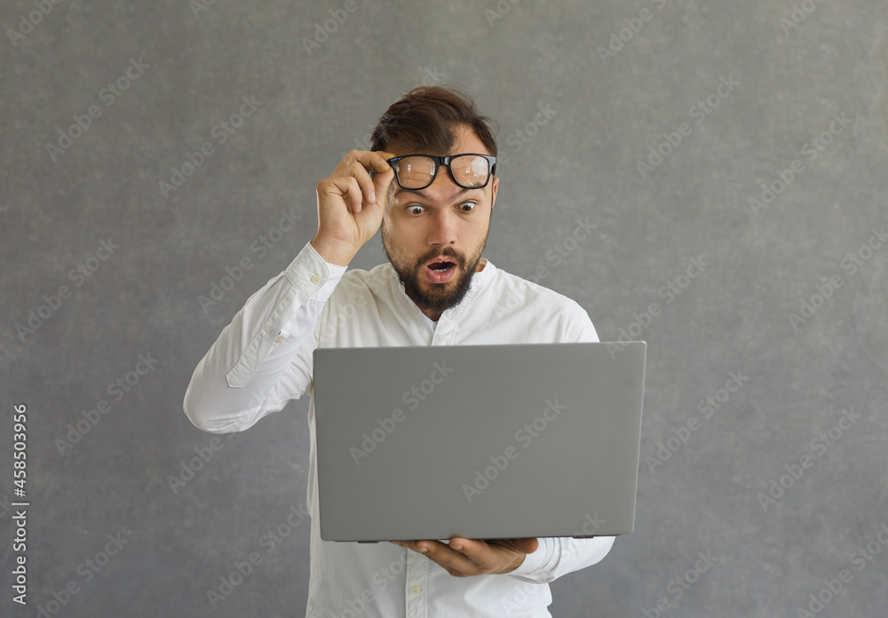 Young man looking at screen of his laptop computer with expression of ...