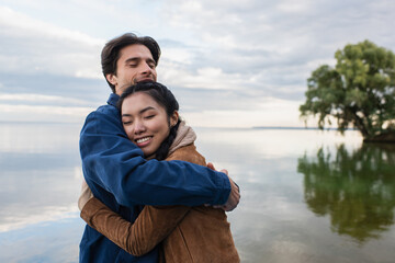 Wall Mural - man embracing asian girlfriend near lake