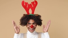 Surprised Merry Young Santa Curly African American Man 20s In White Shirt Christmas Hat Raindeer Antlers Red Nose Look Around Spreading Hands Isolated On Plain Pastel Beige Background Studio Portrait