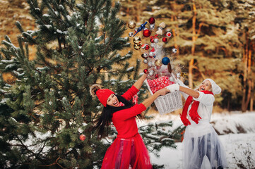 two girls near the Christmas tree throw a lot of toys on the tree. Christmas tree decoration on the street in winter.Lots of Christmas balls on the tree