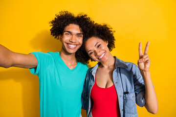 Photo of happy charming young dark skin couple make selfie v-sign smile isolated on yellow color background