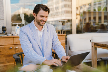 Young man wearing jacket working with laptop while sitting at cafe