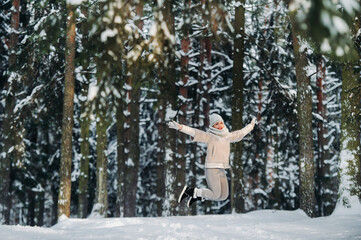 a woman in gray clothes jumps emotionally in a winter forest.Girl in the new year's snow-covered forest.