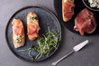 Italian appetizer of bread and prosciutto, crostini with ham, ricotta and microgreens on a gray background.